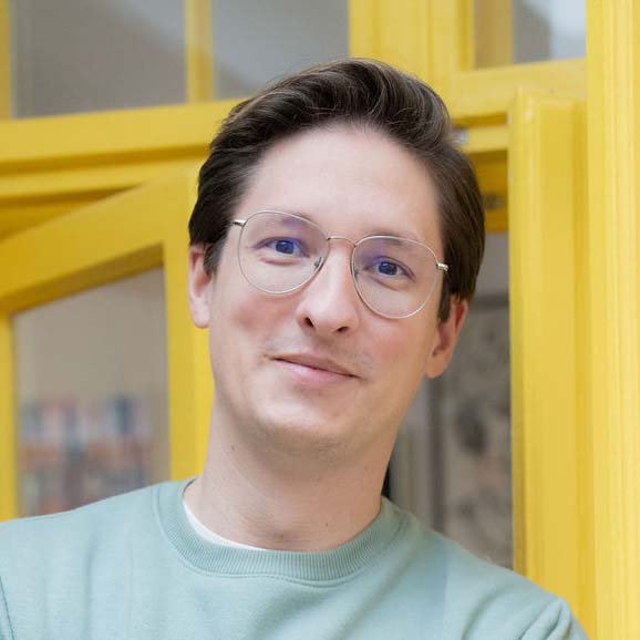 Porträt eines lächelnden Mannes mit Brille vor gelbem Türrahmen.